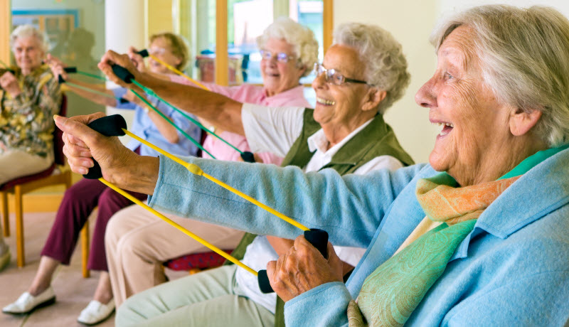 Large group of happy enthusiastic elderly ladies exercising in a gym sitting in chairs