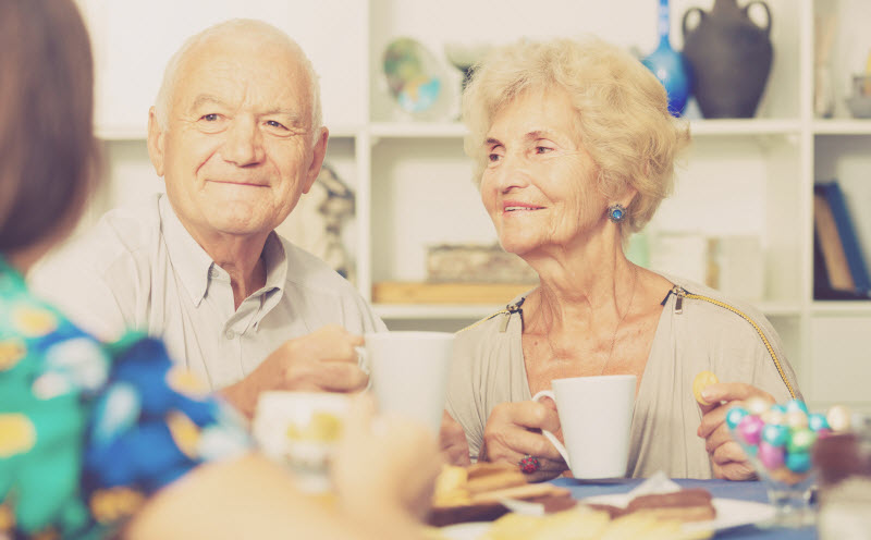 Happy senior couple enjoying conversation with female over cup of coffee
