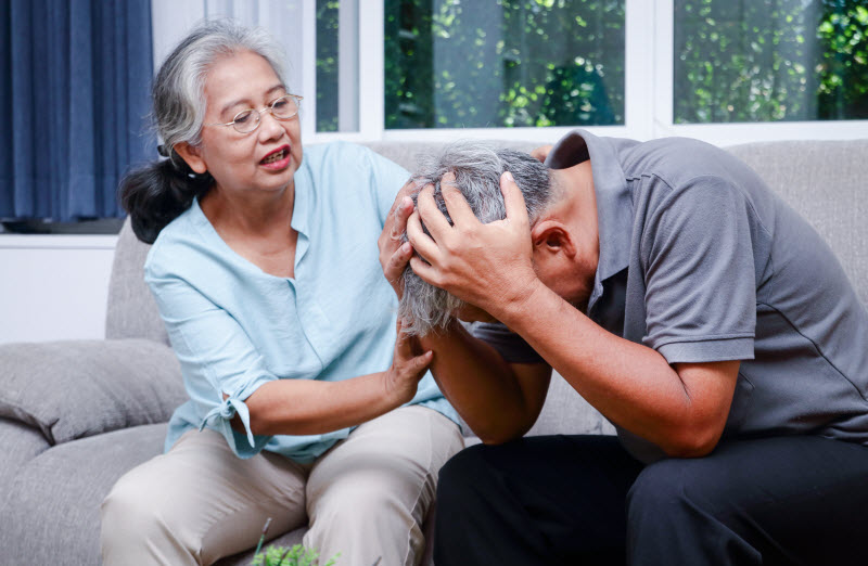 A sick Asian elderly man put his hand on his head while wife is worried