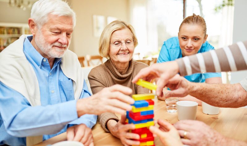 Group of seniors plays together with colorful building blocks in retirement home