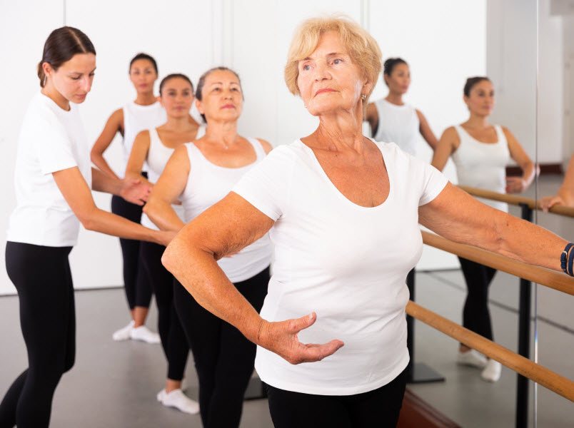 Elderly woman doing ballet steps at ballet barre in the dance studio